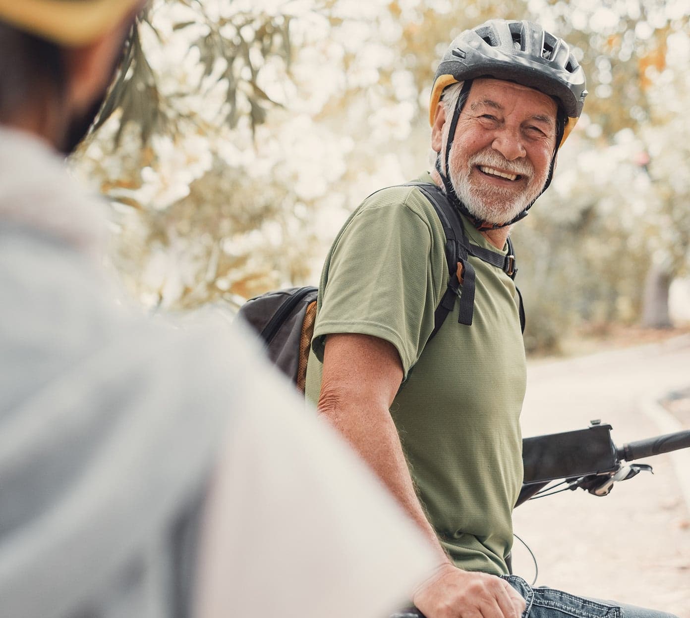 A mature man wearing a bicycle helmet is looking back and smiling